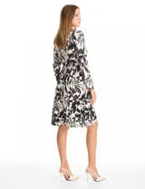 Vestido corto de seda fría con estampado botánico en blanco y negro. Presenta escote en V cruzado, mangas largas entalladas, cintura elastizada con aplique metálico lateral y ruedo asimétrico.