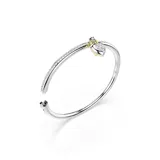 Brazalete rígido de la colección Idyllia, con diseño de media caña adornado con cristales transparentes. Presenta un dije central en forma de corazón tipo medallón, con baño en tono oro y una zirconia rosa en una cara, y pavé de cristales con baño de rodio en la otra.