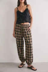 Pantalón baggy de tiro medio con estampado a cuadros en tonos beige, tostado y negro, confeccionado en algodón peinado. Presenta cintura elástica con cordón de ajuste y puños elastizados en los tobillos.