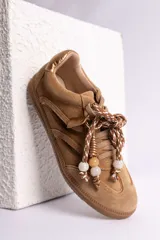 Zapatillas urbanas de gamuza color marrón, con diseño de cordones decorados con cuentas de piedra y detalles de líneas brillantes en los laterales. Presentan suela de goma texturizada al tono.