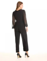 Enterito negro de seda fría con escote en V cruzado, mangas largas voluminosas de gasa transparente con puños elásticos fruncidos. Tiene cintura elástica interna, lazo lateral ajustable y pierna de corte recto al tobillo.