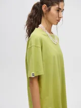 Remera de corte cuadrado y ajuste holgado, color verde oliva, con pequeño estampado gráfico de un velero en el pecho y etiqueta decorativa en la manga.