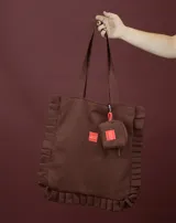 Tote bag color amarillo con diseño de volados en los laterales y la base. Cuenta con doble asa larga para llevar al hombro y una etiqueta roja pequeña con logo en el centro.