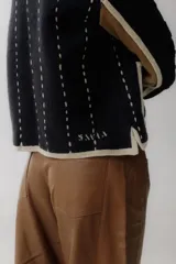 Chaqueta de punto con diseño color block en negro, beige y marrón. Presenta cuello redondo, cierre frontal con botones grandes, bolsillos frontales y detalles de costuras decorativas verticales en color claro.