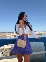 Bandolera pequeña color beige, confeccionada en cuero sintético de acabado suave. Presenta dos compartimentos principales con cierre y una correa ajustable de tela con diseño geométrico estampado.