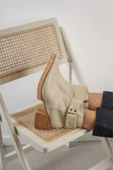 Bota corta de cuero negro con acabado combinado mate y charol. Presenta una tira decorativa con tachas metálicas y hebilla en el tobillo, tacón cuadrado robusto y suela con plataforma.