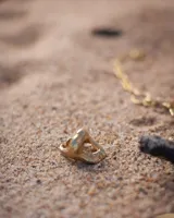 Anillo plateado con forma orgánica irregular y un agujero en el centro.