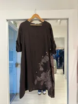 Vestido midi de lino color marrón chocolate, con cuello redondo, mangas tres cuartos y detalle de botonadura diagonal en el frente con estampa floral en la parte inferior.