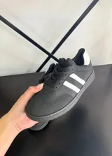 Championes estilo urbano color negro con dos franjas blancas laterales, detalle blanco en el talón, suela de goma texturizada y cordones negros.