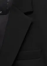 Blazer negro de corte entallado, con cuello de solapa con muesca, hombros estructurados, cierre frontal de un botón, bolsillos de ribete delanteros y manga larga.