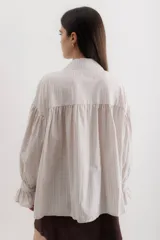 Camisa celeste a rayas verticales blancas, con cuello clásico, cierre frontal con botones y mangas largas abullonadas con puños elásticos.