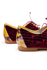Zapatos tipo oxford de terciopelo rayado en color granate, con detalles de cuero con estampado de piel de serpiente en el talón y la puntera. Presentan cordones finos y ribetes en color amarillo.