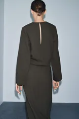 Vestido midi de Zara Woman Collection, color verde oscuro, con cuello redondo, manga larga y detalle de pliegues en el delantero. Presenta un corte recto con abertura frontal en el bajo y cierre lateral con cremallera oculta.