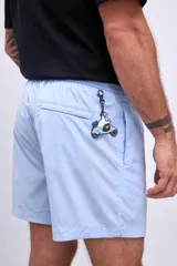 Short de baño color celeste, con cordón ajustable en la cintura y un parche cuadrado negro con el logo "HAUS" en blanco en la pierna izquierda.