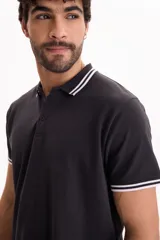 Chomba de piqué color negro con cierre frontal de botones, cuello y puños acanalados con líneas blancas contrastantes.
