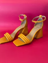 Sandalias de cuero color mostaza, con tira delantera doble y pulsera al tobillo con hebilla. Taco geométrico de 8,5 cm.