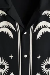Camisa de manga corta de H&M, con corte relajado, cuello abierto estilo resort, tapeta frontal con botones y bajo recto. Diseño estampado en color blanco sobre base negra con motivos de palmeras, soles y estrellas.