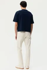 Pantalón chino de sarga elástica de algodón, con cierre de cremallera y botón, bolsillos laterales al bies y bolsillos traseros con botón. Presenta un corte ajustado que define la silueta.