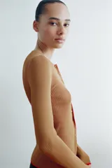 Chaqueta de punto marrón con cuello redondo, manga larga y ribetes en color rojo. Cuenta con cierre frontal de botones.