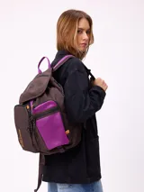 Mochila urbana marca Rusty de color negro, con múltiples compartimentos frontales, bolsillo de red lateral y detalles en azul y amarillo. Presenta el logo de la marca en la solapa superior y el texto 'Rusty Worldwide' en el frente.