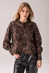 Camisa de manga larga con estampado floral en tonos marrón y negro. Presenta un diseño con volados estructurados en el frente y cuello, pliegues verticales en el pecho, mangas abullonadas y puños con botones.