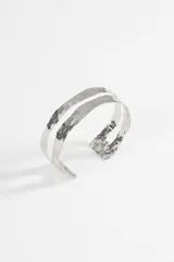 Brazalete rígido de diseño abierto con doble banda, acabado plateado y textura martillada.
