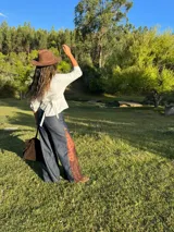 Pantalón de jean estilo wide leg, confeccionado en denim rígido de color azul oscuro. Presenta paneles laterales de encaje con diseño floral en tono rojizo y terminaciones deshilachadas en el ruedo.