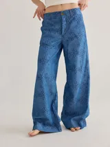 Pantalón de jean de corte ancho y tiro medio, con estampado de monograma en color azul oscuro sobre base de denim azul claro. Presenta cierre frontal con botón y costuras a la vista.