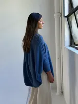 Poncho de tejido de punto color azul jean, con cuello alto y diseño de trenzas verticales. Presenta mangas integradas con puños acanalados y corte holgado.