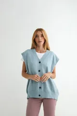 Chaleco de punto color celeste, con escote en V y cierre frontal de botones negros. Presenta un diseño holgado con terminaciones acanaladas en el cuello, sisas y ruedo.
