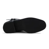 Bota de cuero negra de caña baja, con taco cuadrado y punta fina. Presenta una correa con hebilla alrededor del tobillo y un aplique metálico en el lateral. Cuenta con cierre lateral.