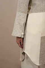 Camisa larga de lana fina sin teñir, con cuello mao y cierre frontal con un botón. Presenta un diseño de patchwork en tonos beige y gris con patrones de pata de gallo y texturas lineales. Las mangas son largas con tajo y detalle de botón en los puños.