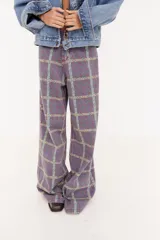 Pantalón de corte recto y tiro medio con estampado geométrico en tonos amarillos, verdes y violetas. Presenta un diseño de líneas verticales que forman cuadros y un patrón repetitivo de letras.