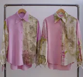 Camisa blanca con estampado de hojas en tonos beige y verde, cuello camisero, mangas largas con lazos en los puños y botones de madera.