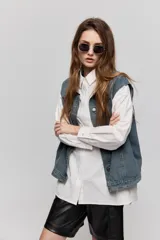Chaleco de jean azul con sutil textura a rayas, cuello camisero, cierre frontal con botones metálicos y diseño sin mangas con hombros amplios.