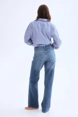 Jeans de cinco bolsillos en denim de algodón con leve stretch, de tiro alto y corte ajustado desde la cintura hasta el muslo, ensanchándose de la rodilla hacia abajo (bootcut). Presenta cierre y botón frontal.