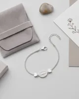 Pulsera de acero con baño de plata, con dije central ovalado de la Virgen Milagrosa y dos pequeños dijes en forma de corazón a los costados.