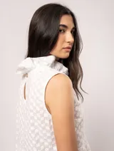 Blusa blanca sin mangas, con cuello alto con volados y detalles bordados con motivos florales.