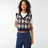 Chaleco de punto sin mangas, con cuello en V, de estilo argyle en tonos azul marino, beige, gris y blanco. Se muestra sobre una camiseta blanca de manga corta y un pantalón azul marino.