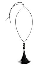 Collar largo con cordón negro y colgante compuesto por cuentas de diferentes materiales y colores (verde, negro y perla) rematado con una borla de flecos negros.