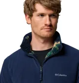 Campera polar de textura tipo corderito con estampado camuflado en tonos verde, azul marino y beige. Presenta cierre frontal completo, cuello alto y un bolsillo frontal en el pecho con cierre y parche de la marca.