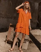 Vestido camisero de lino color naranja, con mangas cortas, cierre frontal de botonadura y diseño asimétrico con volados en el ruedo.