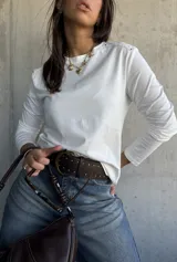 Remera de manga larga color blanco, con cuello redondo y detalle de tachas metálicas en los hombros.
