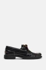 Zapato tipo náutico de piel color negro, con detalle de pespuntes en contraste, cordones decorativos y puntera redonda con costura fruncida.