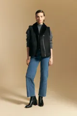 Chaleco negro de gamuza sintética con interior y bordes de corderito sintético. Presenta un diseño sin mangas con cuello solapa y cierre frontal.