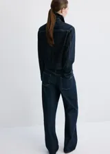 Chaqueta corta de denim en color azul oscuro, con cuello clásico, cierre frontal con botones, mangas largas y un bolsillo aplicado en el pecho.