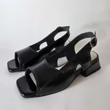 Sandalias de cuero negro con textura sutil, diseño destalonado con aberturas laterales, puntera cuadrada y taco bajo cuadrado. Cuenta con tira ajustable en el talón con hebilla metálica.