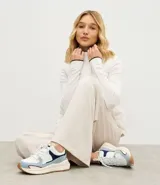 Championes estilo jogging con diseño de recortes contrastantes en tonos blanco, azul y gris. Presenta una parte superior de mesh respirable con sobreposiciones de poliuretano, forro suave y suela robusta de color crema con base marrón.