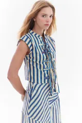 Blusa sin mangas de algodón con estampado de rayas en tonos beige, azul y rojo. Presenta diseño de inspiración oriental con cierre frontal de múltiples lazos para atar.