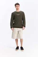 Sweater oversize verde militar de tejido liviano, con hombros caídos, cuello redondo, costuras a la vista y bordado sutil en el pecho.
